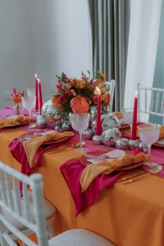 the table is set with orange and pink linens, silverware, candles, and flowers