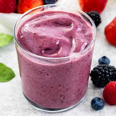 a smoothie in a glass with berries around it