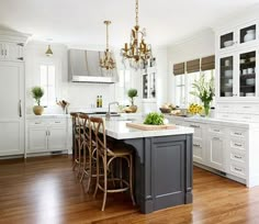 a large kitchen with white cabinets and wooden floors is pictured in this image, there are several chairs around the island