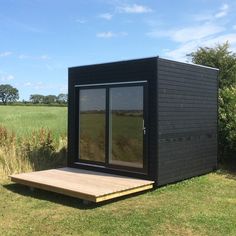 a small black building sitting on top of a grass covered field next to a wooden platform