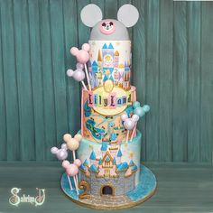 a three tiered cake with mickey mouse decorations on it's side and balloons in the air