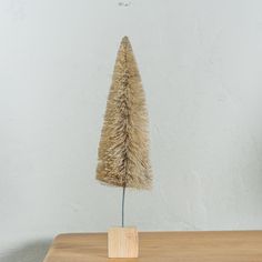 a small tree made out of straw on a wooden table in front of a white wall