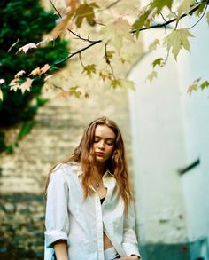 a woman standing in front of a tree with her hand on her hip and looking down