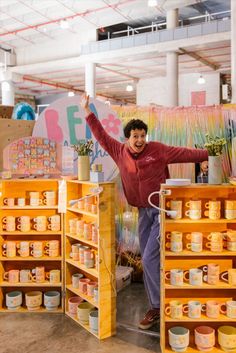 a man is standing in front of some shelves with jars on them and flowers behind him