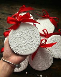 a hand holding four white ceramic ornaments with red bows