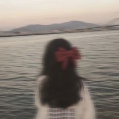 a woman with a red bow on her head standing in front of the water