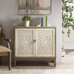 a white cabinet sitting next to a chair and potted plant on top of a table