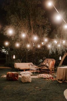 an outdoor seating area is lit up with string lights and blankets on the grass at night