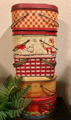 a stack of colorful tins sitting on top of a table next to a plant