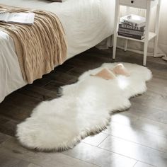 a white sheepskin rug on the floor next to a bed with pillows and blankets