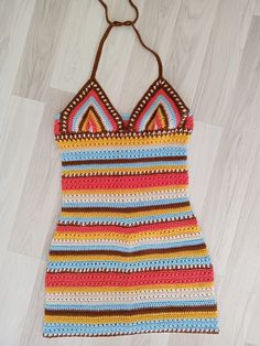 a colorful crocheted dress hanging on a wooden hanger with white wood flooring