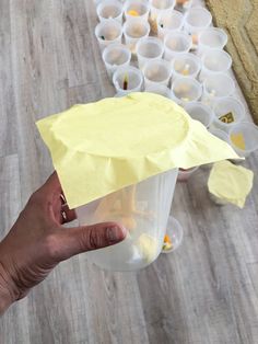 a hand holding a yellow piece of paper over a container filled with plastic cups on a wooden floor