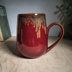 a red and gold coffee mug sitting on top of a table next to a book