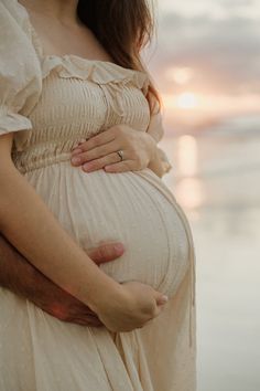 a pregnant woman is holding her husband's belly while the sun sets in the background