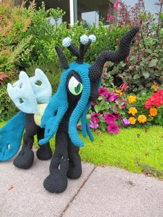 two crocheted stuffed animals sitting next to each other in front of some flowers