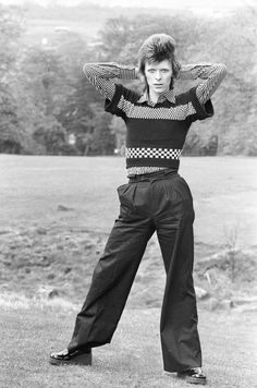 an old black and white photo of a man with his hands on his head, standing in the grass