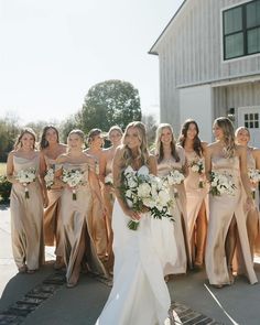 a group of women standing next to each other in front of a white barn holding bouquets