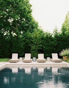 a pool with lounge chairs next to it and trees in the backgroung