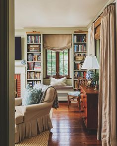 a living room filled with furniture and bookshelves next to a window covered in curtains