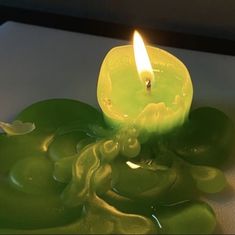 a green candle sitting on top of a white table next to some grapes and leaves