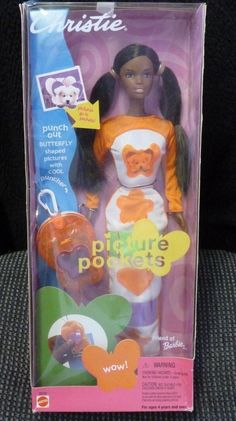 the doll is in its box and it has an orange bear on her chest,