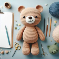 a crocheted teddy bear sitting on top of a table next to yarn and scissors