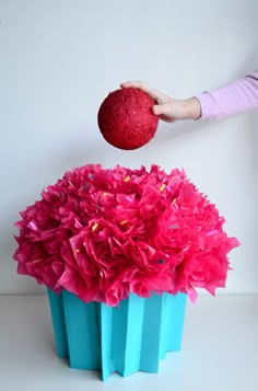 a red ball is being thrown into a blue cup with pink flowers in it and someone reaching for it