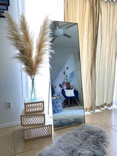 a large mirror sitting on top of a floor next to a vase filled with dry grass