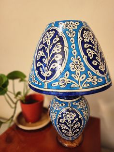 a blue and white lamp sitting on top of a table next to a potted plant