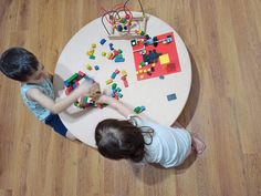 two children playing with legos on the floor in front of a round wooden table