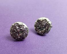 two silver and black earrings sitting on top of a purple surface