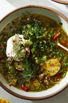 a white bowl filled with soup and vegetables on top of a table next to lemon wedges