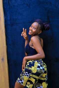 a woman standing in front of a blue wall giving the peace sign with her hand