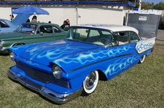 an old blue car with flames painted on it's side at a car show