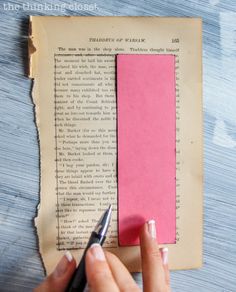 a person cutting out a piece of pink paper with a pen on top of it