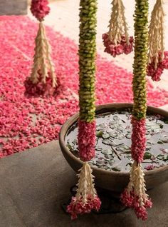 pink and white flowers in a pot with water on the ground next to it, surrounded by petals