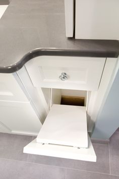 an open cabinet door in a kitchen with gray flooring and white cabinets on either side