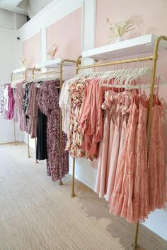 clothes are hanging on racks in a clothing store, with pink walls and carpeting