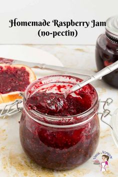 homemade raspberry jam in a glass jar with a spoon on the table next to it