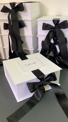 two white boxes with black ribbons tied around the edges and one box has a name on it