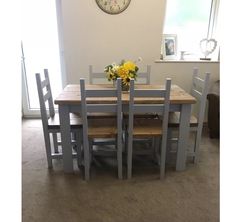 a wooden table with chairs around it and a clock on the wall behind it in a living room