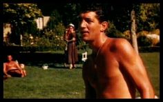 a shirtless man standing in the grass with other people behind him and another person sitting on the ground