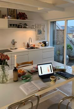 an open laptop computer sitting on top of a kitchen counter next to a table filled with books