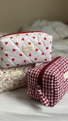 two cosmetic bags sitting next to each other on top of a white sheet covered bed