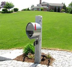 a mailbox is in the middle of a brick path near a grassy field and house