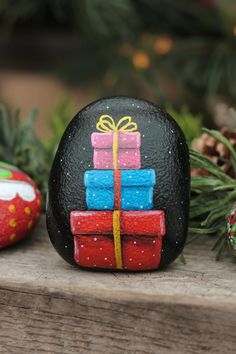 painted rocks with presents on them sitting next to pine cones