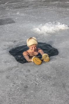 a woman wearing a beanie and mittens in the middle of an icy lake