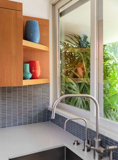 a kitchen sink sitting under a window next to a wooden shelf filled with vases