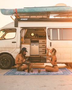 two people sitting on the ground in front of a van