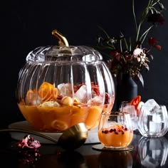 a glass bowl filled with oranges and other food on top of a black table